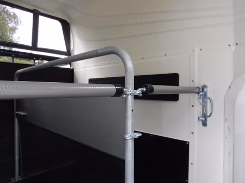 Metallgestell mit Rohren und Halterungen in einem weißen Transportfahrzeug mit schwarzen Regalen und Fenster.