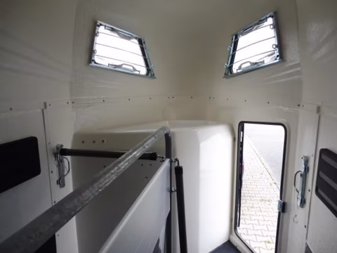 Innenraum eines weißen Transporters mit zwei Dachfenstern, Seitenfenster und offener Tür zum Außenbereich.