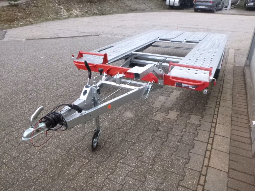 Autoanhänger mit roten Halterungen und silbernem Rahmen auf gepflastertem Parkplatz geparkt.