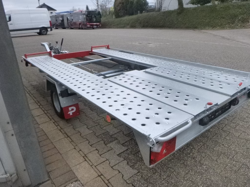 Offener Autotransporter-Anhänger mit Aluminium-Ladefläche und roten Rahmen auf Parkplatz.