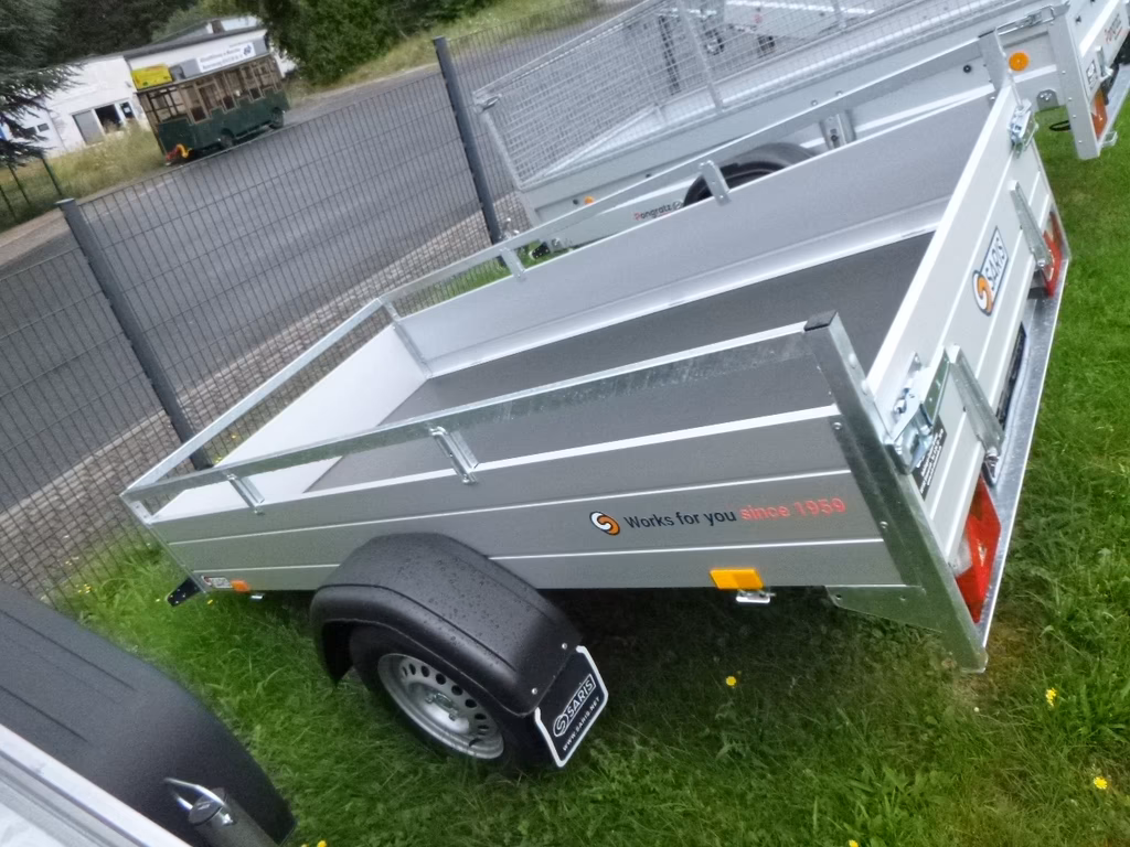 Grüner Anhänger mit weißem Verdeck und "Works for you"-Logo auf Rasen geparkt.