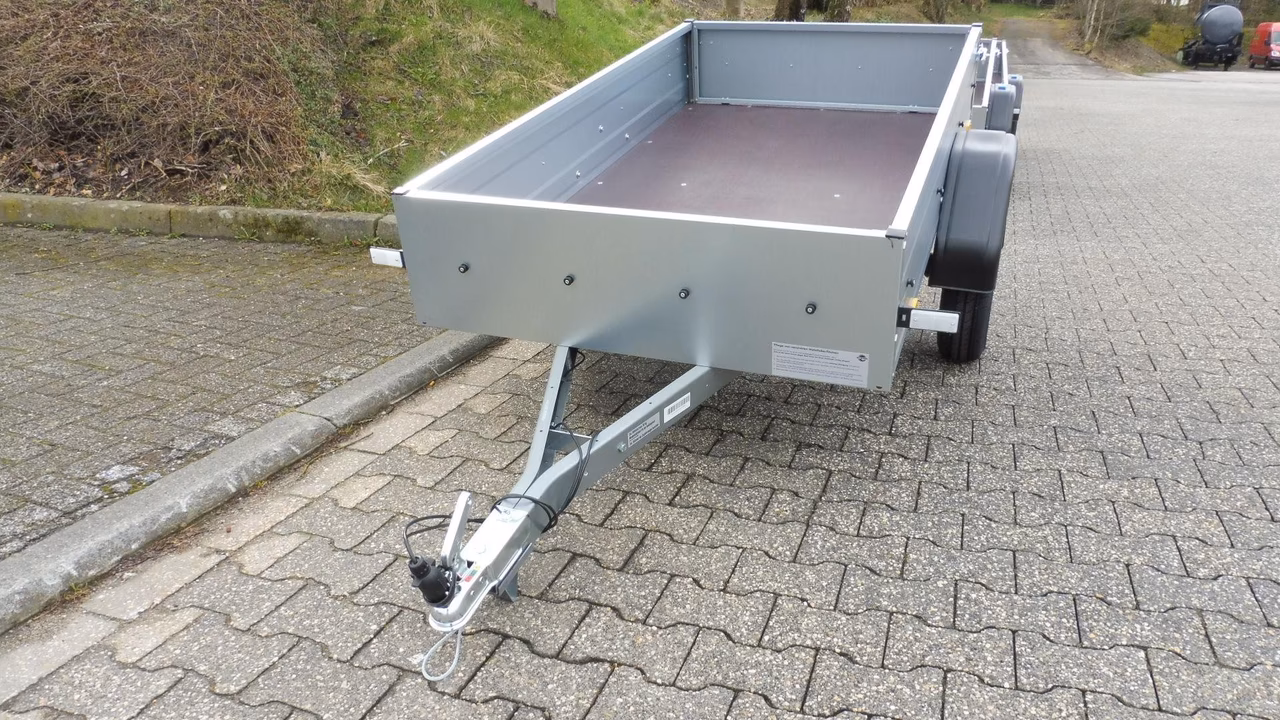 Grauer Transportanhänger mit offener Ladefläche auf gepflastertem Untergrund, Anhängerkupplung sichtbar.