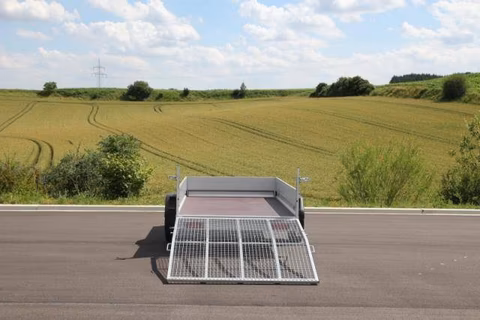 Anhänger mit Solarmodulen auf Straße vor Ackerland und Himmel mit Wolken.