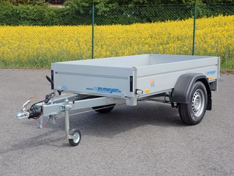 Grauer Einachsanhänger mit hochklappbaren Seitenwänden von Meyerufer auf Asphalt vor gelbem Rapsfeld.