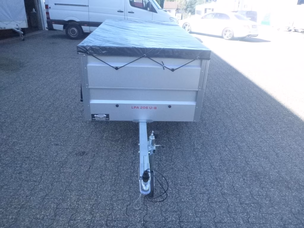 Silbergrauer Anhänger "LPA 206 U-B" mit blauer Plane auf Parkplatz, Zugmaul sichtbar.