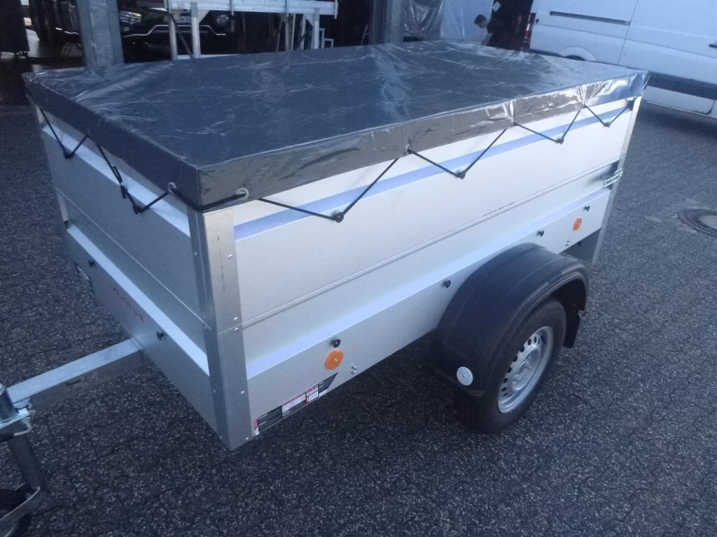Weißer Anhänger mit grauer Abdeckplane und blauen Spanngurten auf Parkplatz geparkt.