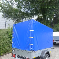 Kleiner Anhänger mit blauer Plane und Spannvorrichtungen auf gepflastertem Untergrund vor grünen Bäumen.