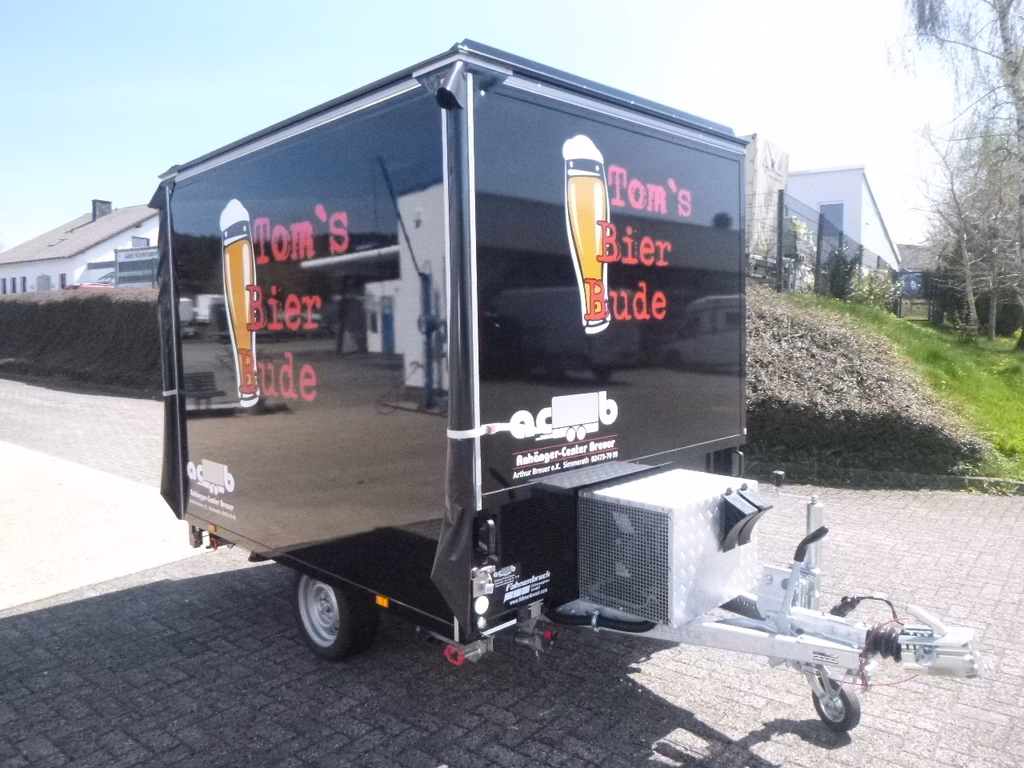 Schwarzer Verkaufsanhänger mit "Tom's Bier Bude" Branding und Bierflasche-Logo auf Parkplatz.