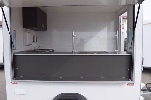 Verkaufsstand mit Theke, Spülbecken und schwarzem Schiebefenster für Straßenverkauf.