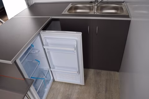 Offene Kühlschranktür in moderner Küche mit Spüle und schwarzen Unterschränken auf Holzboden.