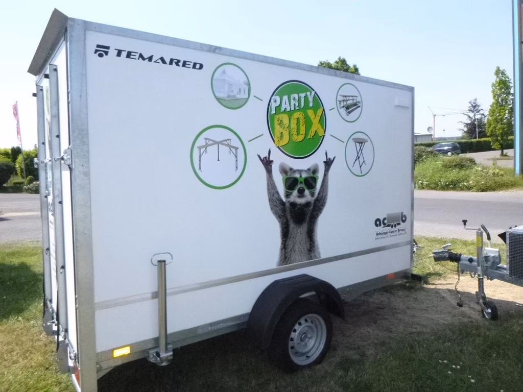 Temared Party Box Anhänger mit Katzen-Motiv und grünen Symbolen für Partyzubehör auf Wiese geparkt.