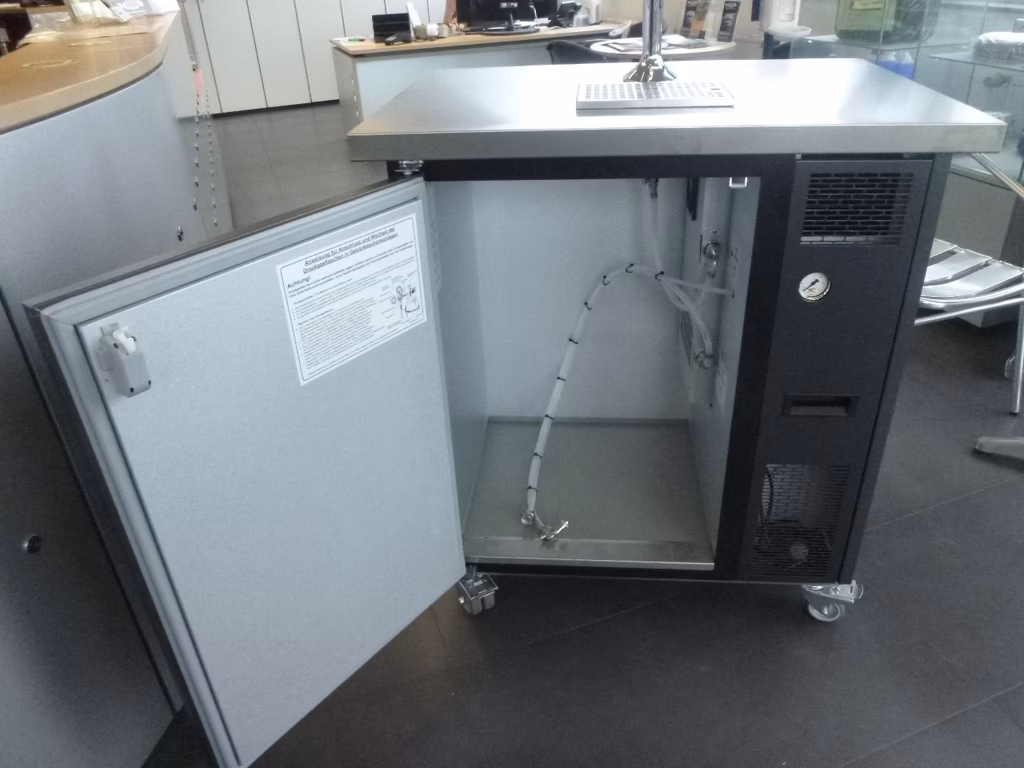 Offener Kühlschrank mit Edelstahltop, schwarzem Kompressor und weißer Tür in Ladenumgebung.