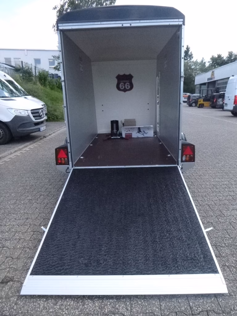 Offener Pferdeanhänger mit Route 66 Schild und ausgeklappter Rampe auf Parkplatz.