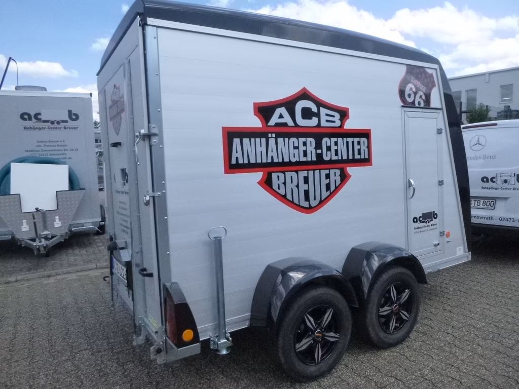 Weißer Anhänger mit ACB Anhänger-Center Breuer Logo und rotem Schriftzug auf Parkplatz.