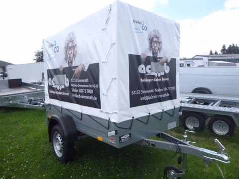 Weißer Verkaufswagen mit schwarzen Bannern auf Rasenplatz, Anhänger mit Unternehmensbranding und Kontaktinformationen.