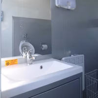Modernes Badezimmer mit weißem Waschbecken, grauem Spiegel und Seifenspender an der Wand.