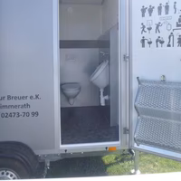 Tragbares WC-Häuschen mit offener Tür, Toilette und Waschbecken sichtbar, auf Rädern montiert.