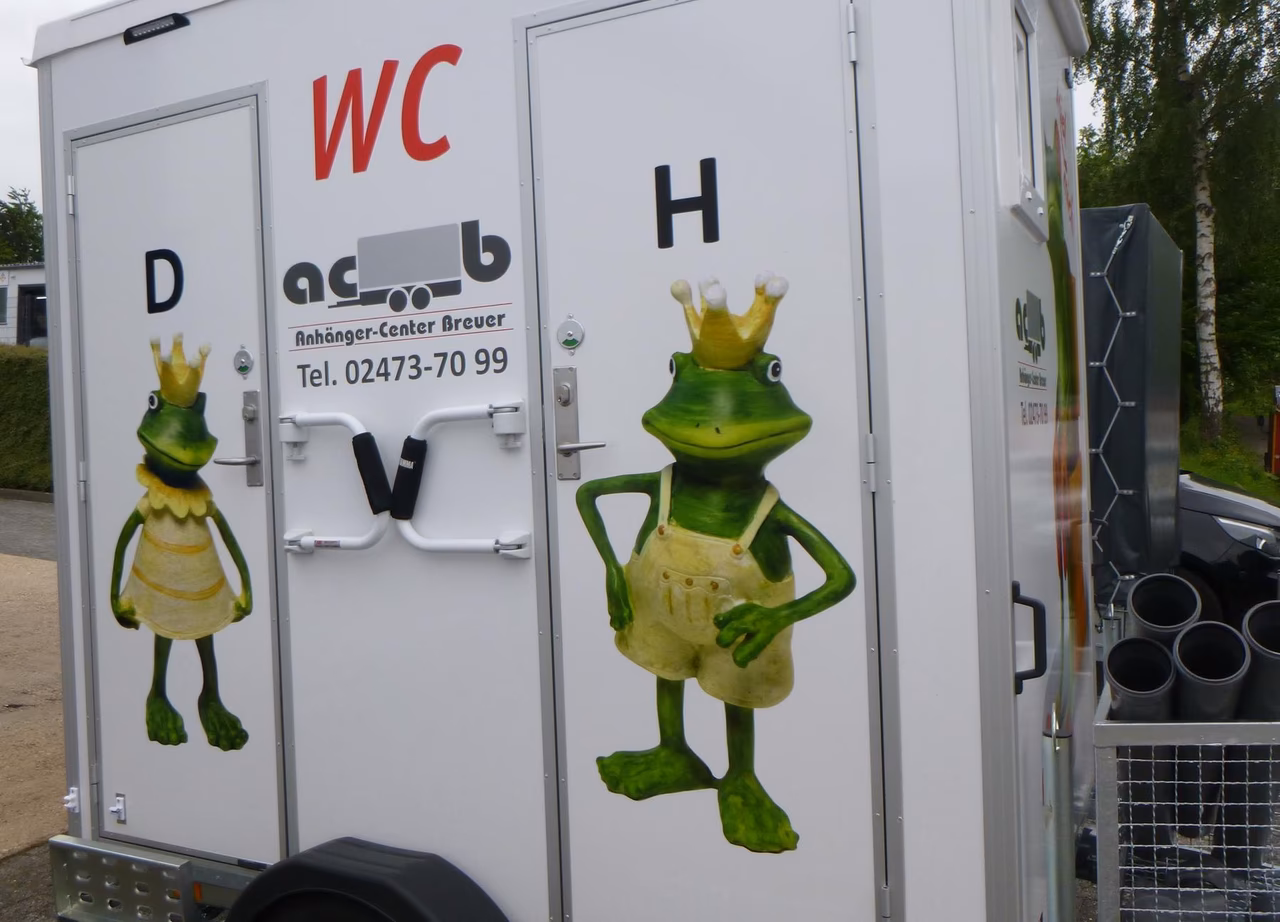Mobiles WC mit grünen Froschfiguren und Schriftzug "Anhänger-Center Breuer"