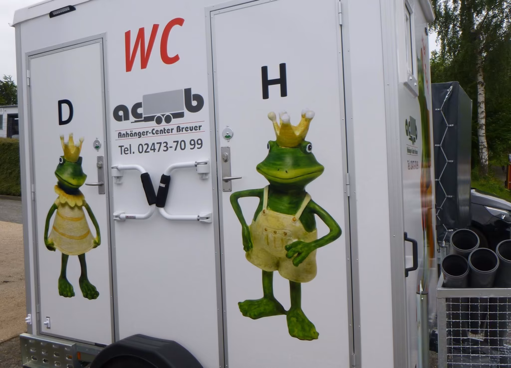 Mobiles WC mit grünen Froschfiguren und Schriftzug "Anhänger-Center Breuer"