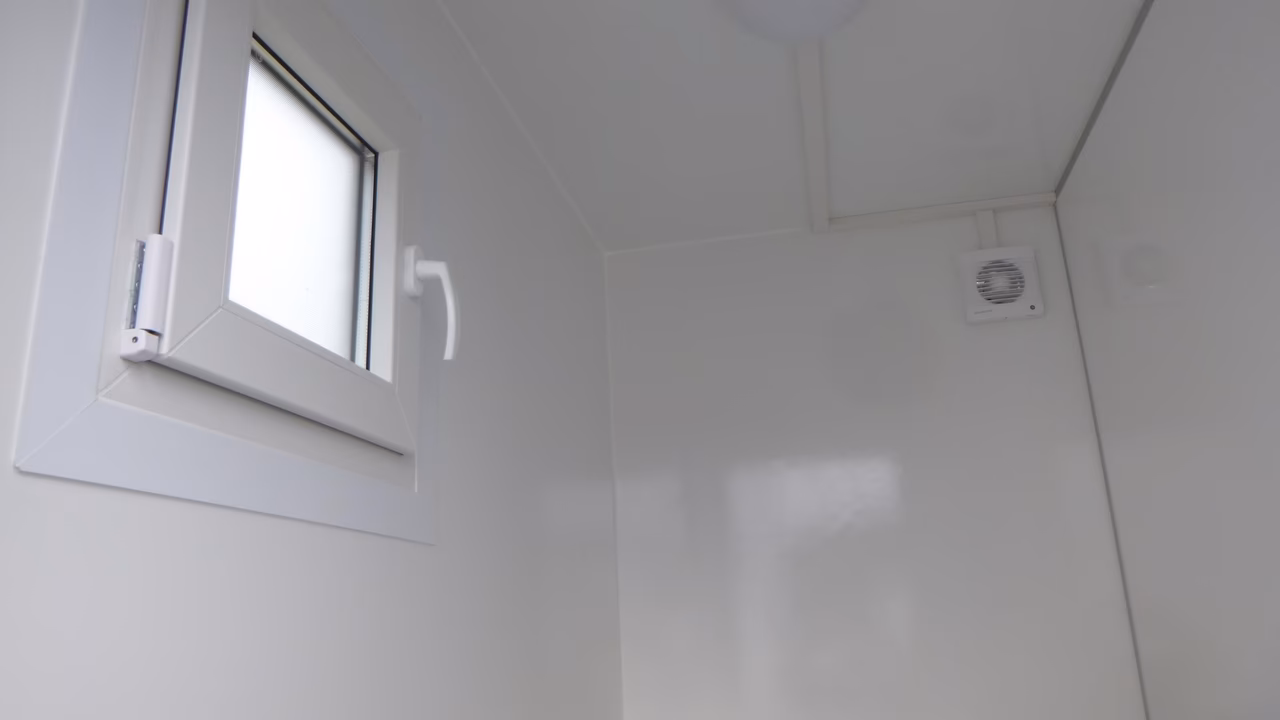 Helles Badezimmer mit kleinem Fenster, weißen Wänden und Lüftungsgitter an der Decke.