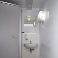 Modernes, schmales Badezimmer mit Waschbecken, Spiegel, Spender und weißer Toilettentür.