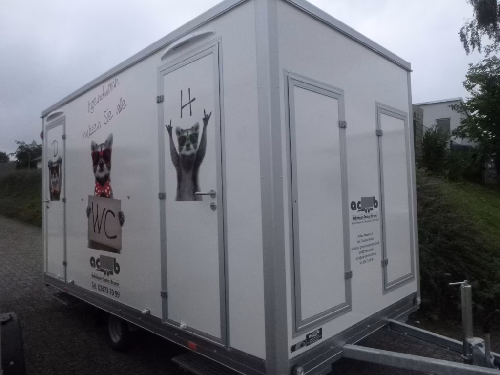 Tragbarer WC-Container mit Katzen-Motiven und WC-Beschriftung auf weißem Anhänger.