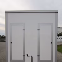 Weiße mobile Toilettenkabine auf Anhänger mit Doppeltüren, Frontansicht auf gepflastertem Untergrund.